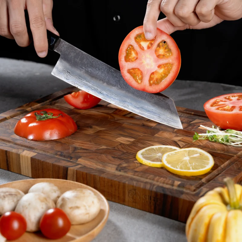 Handgeschmiedetes vietnamesisches Küchenmesser aus Damaststah beim Schneiden von Tomaten auf einem edlen Holzbrett